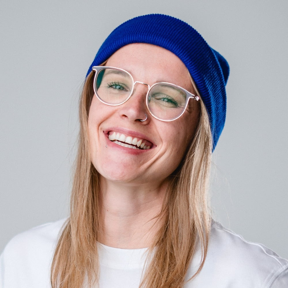 Brenda, Mitgründerin von Gido, mit blauer Mütze und Brille, lächelnd