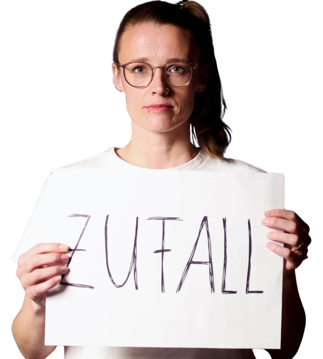 Brenda hält ein handbeschriftetes Schild mit dem Wort "Zufall" hoch